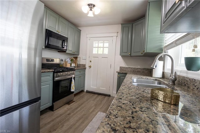 kitchen featuring a sink, gray cabinetry, wood finished floors, stone countertops, and appliances with stainless steel finishes