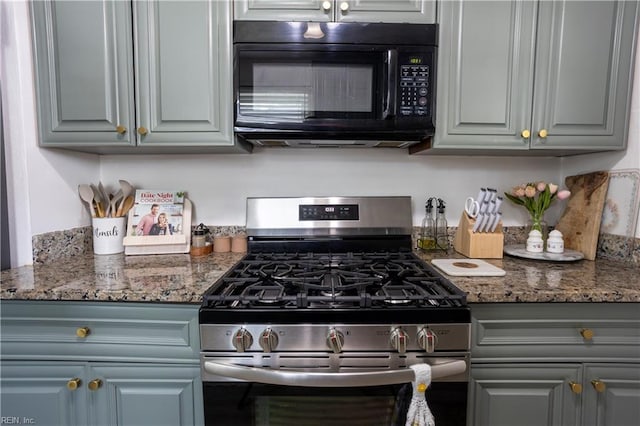 kitchen featuring black microwave, dark stone countertops, gas range, and gray cabinetry