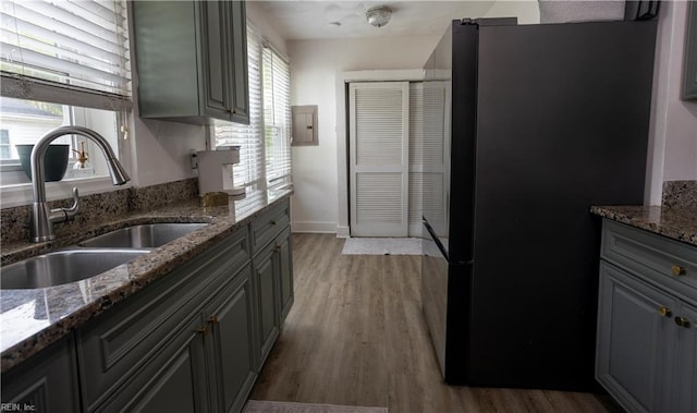 kitchen with wood finished floors, freestanding refrigerator, a sink, and dark stone counters