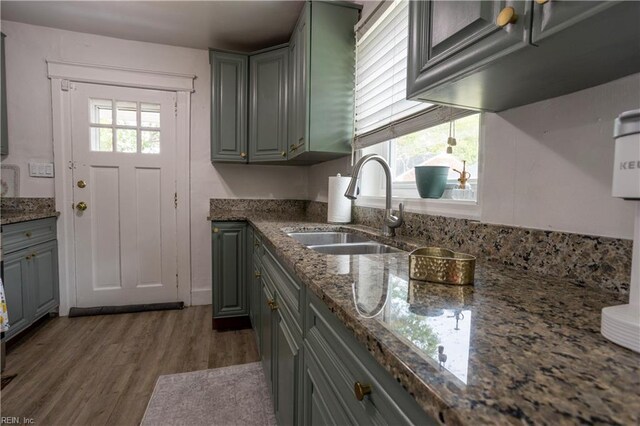 kitchen with gray cabinets, dark stone countertops, wood finished floors, and a sink