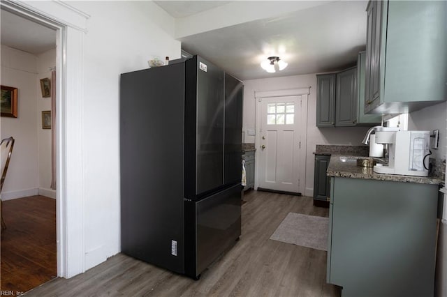 kitchen featuring a sink, freestanding refrigerator, light wood-style floors, gray cabinets, and light stone countertops