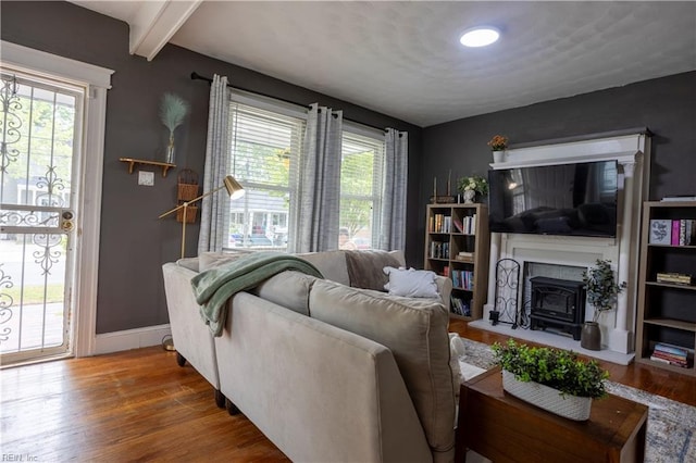 living area featuring beamed ceiling, baseboards, wood finished floors, and a fireplace with raised hearth