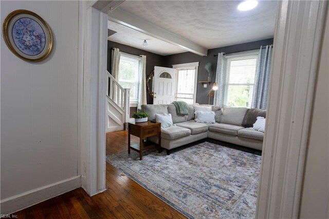 living area featuring a wealth of natural light, beamed ceiling, stairs, and dark wood-style floors