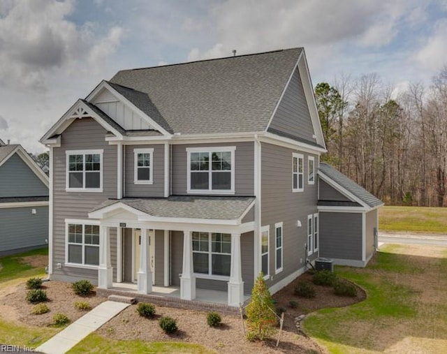 view of front of home with central air condition unit, board and batten siding, covered porch, roof with shingles, and a front yard