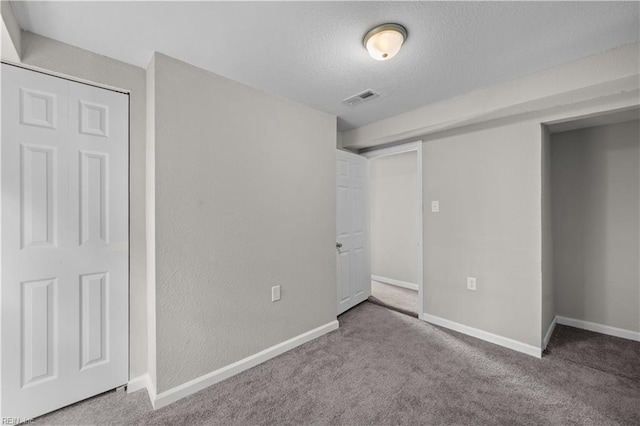 unfurnished bedroom featuring a textured ceiling, carpet, visible vents, and baseboards