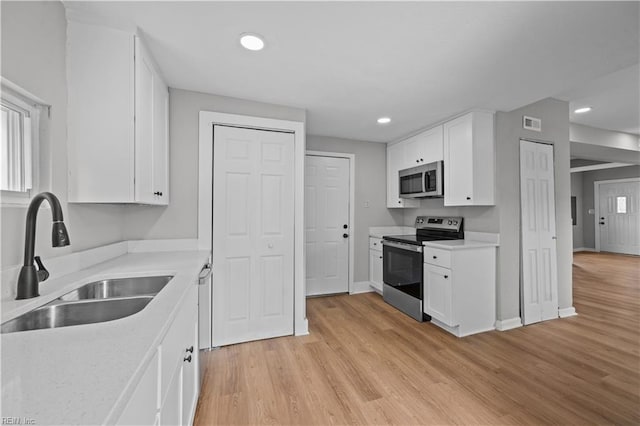 kitchen featuring white cabinets, light wood-type flooring, stainless steel appliances, and a sink
