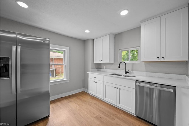 kitchen featuring stainless steel appliances, light countertops, a sink, light wood-type flooring, and white cabinetry