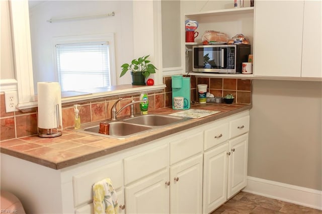 kitchen with stainless steel microwave, tile countertops, decorative backsplash, and a sink