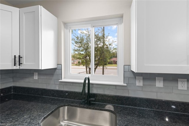 kitchen featuring white cabinets, dark stone countertops, and a sink