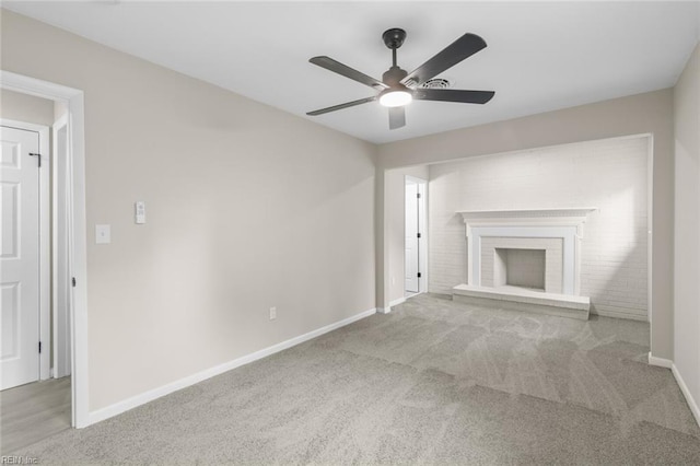 unfurnished living room featuring a brick fireplace, carpet flooring, baseboards, and a ceiling fan