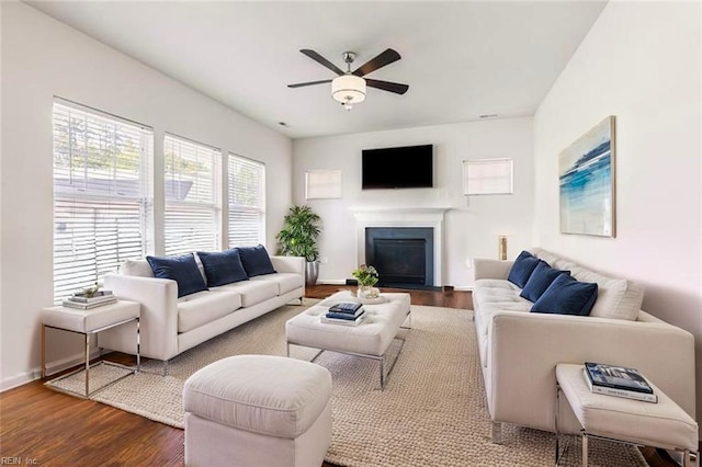 living area with a fireplace with flush hearth, a ceiling fan, baseboards, and dark wood-style flooring
