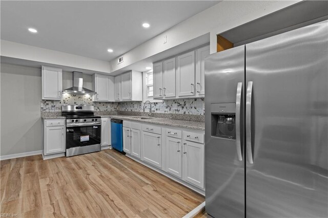 kitchen featuring wall chimney exhaust hood, a sink, light wood-type flooring, decorative backsplash, and appliances with stainless steel finishes