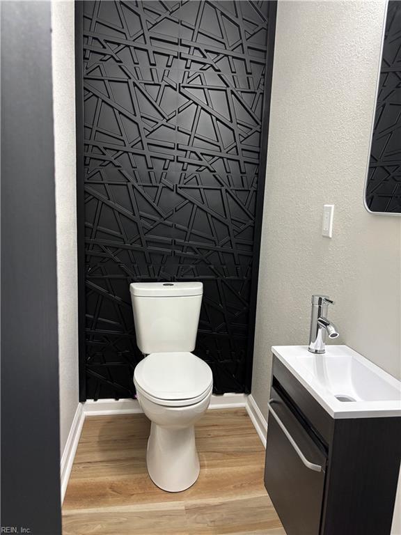 half bath featuring wood finished floors, vanity, toilet, and baseboards