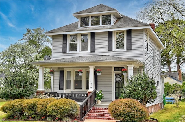 american foursquare style home featuring roof with shingles and a porch