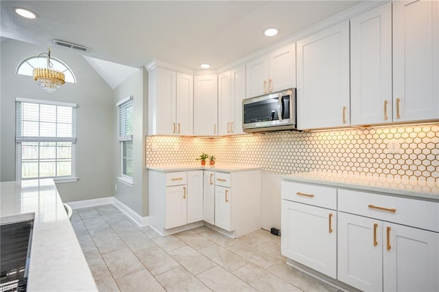kitchen with stainless steel microwave, light countertops, backsplash, and white cabinetry
