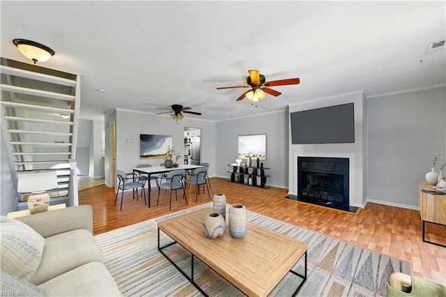 living area with ceiling fan, ornamental molding, light wood-style floors, and a fireplace