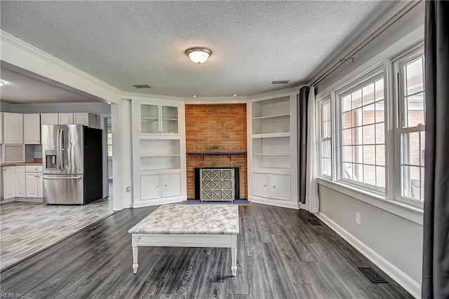 unfurnished living room with a textured ceiling, built in features, baseboards, dark wood-type flooring, and visible vents