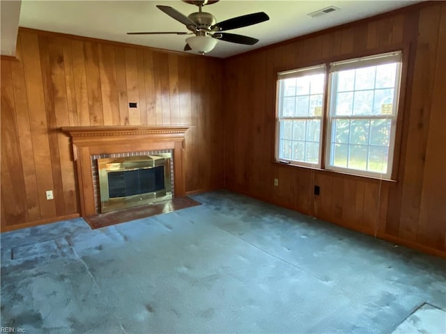 unfurnished living room featuring a fireplace with flush hearth, wooden walls, visible vents, and ceiling fan