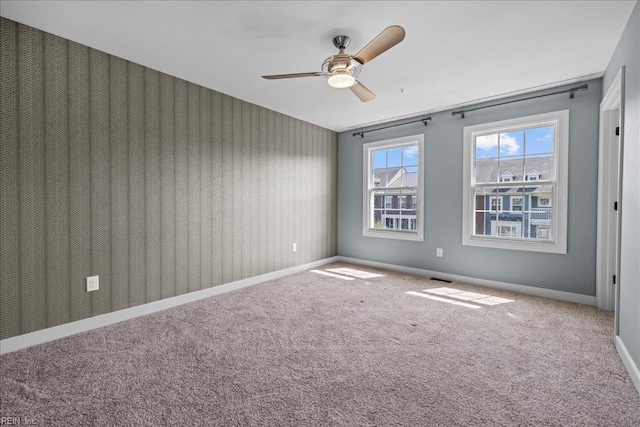 carpeted spare room with ceiling fan, visible vents, and baseboards