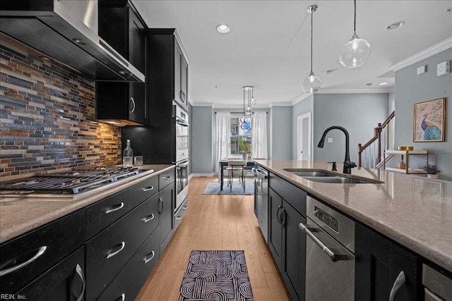 kitchen featuring dark cabinets, appliances with stainless steel finishes, wall chimney range hood, a sink, and crown molding