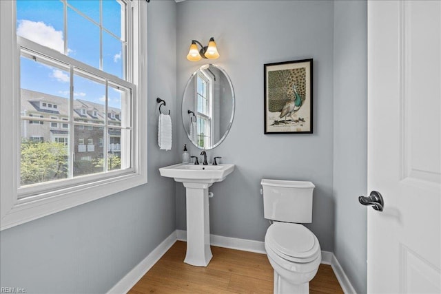 half bathroom with toilet, baseboards, wood finished floors, and plenty of natural light