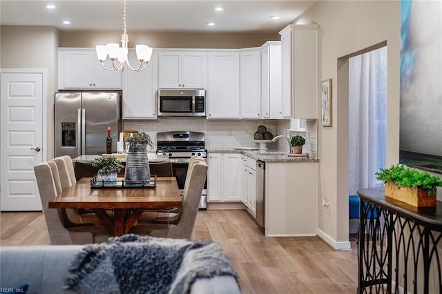 kitchen with stainless steel appliances, backsplash, light wood-style floors, and a chandelier