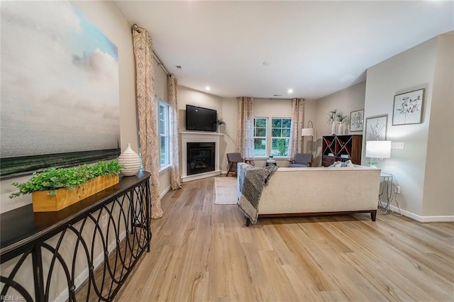 living room featuring light wood-type flooring, baseboards, a glass covered fireplace, and recessed lighting