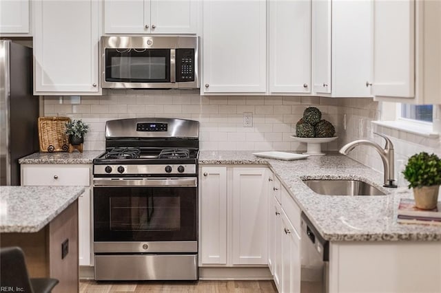 kitchen featuring white cabinets, stainless steel appliances, light stone countertops, and a sink