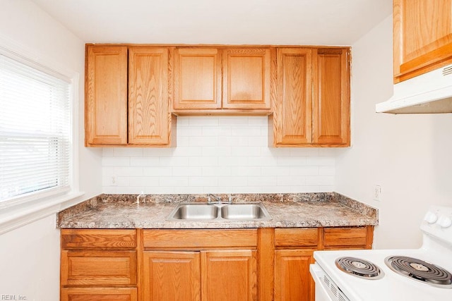 kitchen featuring under cabinet range hood, backsplash, a sink, white range with electric cooktop, and brown cabinetry