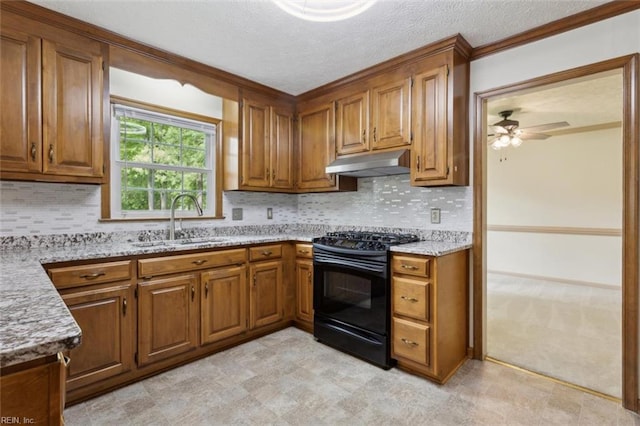 kitchen with a sink, gas stove, brown cabinets, ceiling fan, and under cabinet range hood