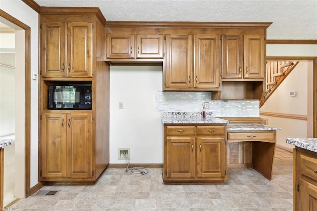 kitchen featuring a textured ceiling, baseboards, backsplash, brown cabinets, and black microwave