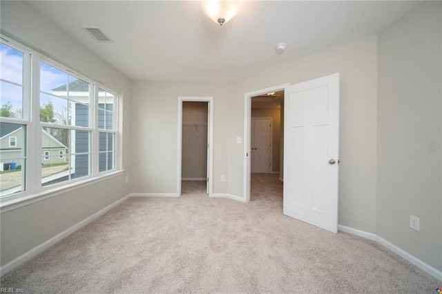 unfurnished bedroom with a spacious closet, baseboards, visible vents, and light colored carpet