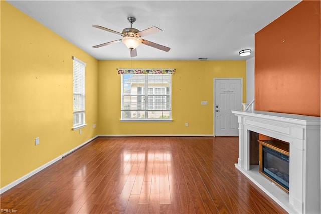 unfurnished living room featuring a glass covered fireplace, wood finished floors, baseboards, and ceiling fan