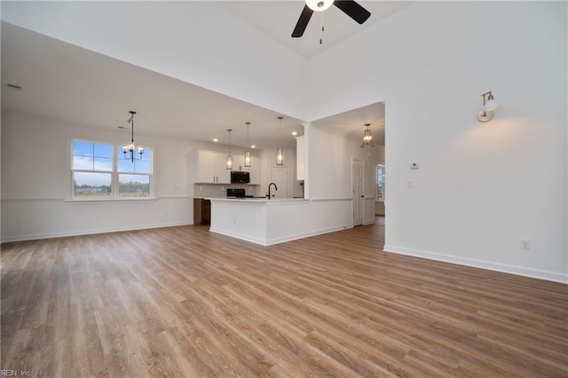 unfurnished living room with baseboards, wood finished floors, a high ceiling, and ceiling fan with notable chandelier