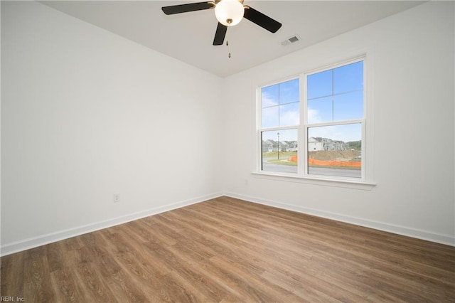 spare room featuring wood finished floors, visible vents, a ceiling fan, and baseboards