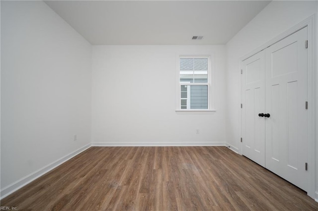 unfurnished bedroom featuring baseboards, wood finished floors, and visible vents