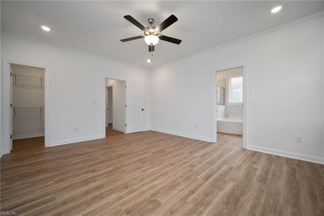 unfurnished bedroom featuring crown molding, wood finished floors, ensuite bathroom, a walk in closet, and baseboards