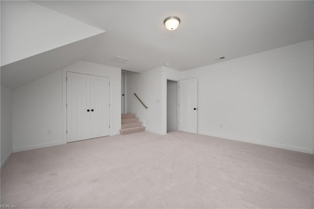 additional living space featuring light colored carpet, baseboards, visible vents, and stairway