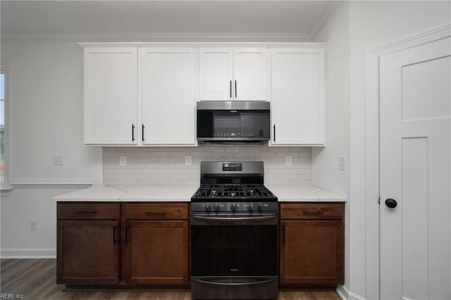 kitchen with stainless steel microwave, tasteful backsplash, white cabinetry, gas range oven, and wood finished floors