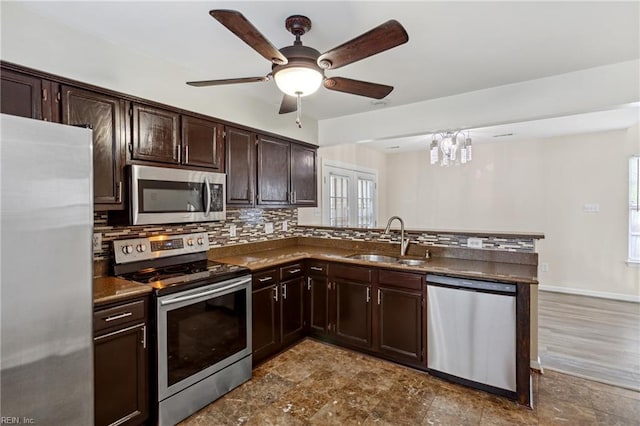 kitchen with stainless steel appliances, a peninsula, a sink, dark countertops, and decorative backsplash