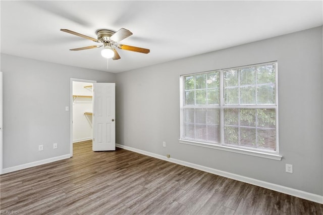unfurnished bedroom with baseboards, a ceiling fan, wood finished floors, and a spacious closet