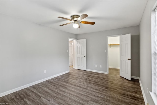 unfurnished bedroom with dark wood finished floors, baseboards, a ceiling fan, a closet, and a walk in closet
