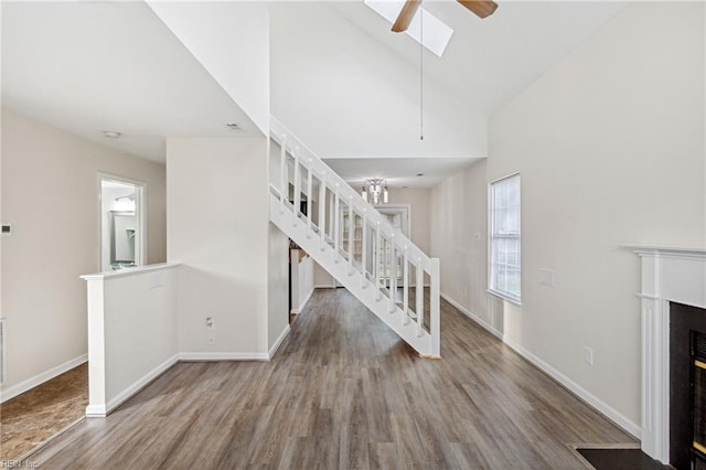 unfurnished living room featuring a fireplace with flush hearth, wood finished floors, stairway, ceiling fan, and high vaulted ceiling