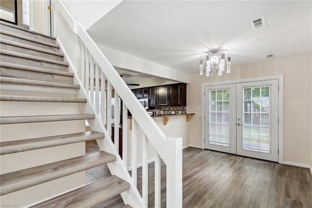 staircase featuring wood finished floors, french doors, a chandelier, and visible vents