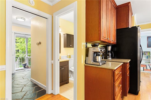 kitchen featuring brown cabinets, light wood finished floors, light stone counters, freestanding refrigerator, and crown molding