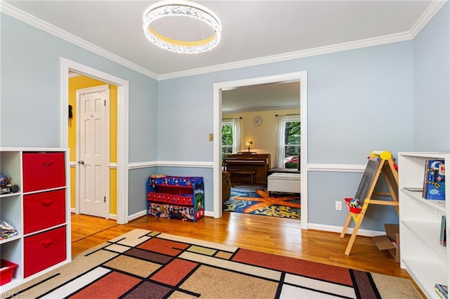recreation room with wood finished floors, baseboards, and ornamental molding