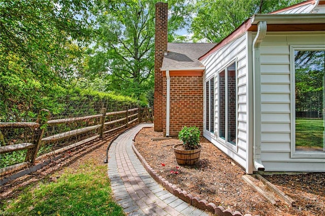 view of property exterior featuring a chimney, fence, and brick siding