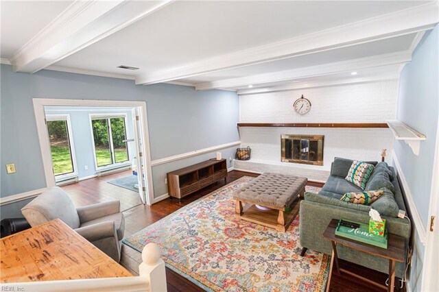 living room featuring visible vents, beamed ceiling, a brick fireplace, wood finished floors, and crown molding