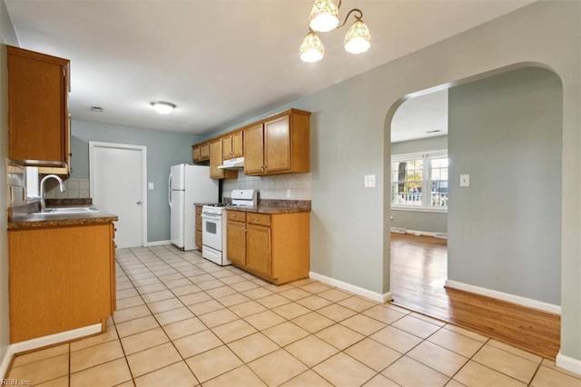 kitchen featuring arched walkways, a sink, dark countertops, backsplash, and white appliances