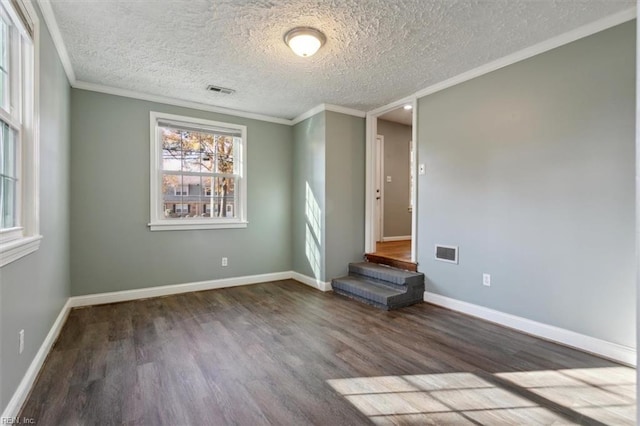 empty room with wood finished floors, visible vents, a textured ceiling, and crown molding